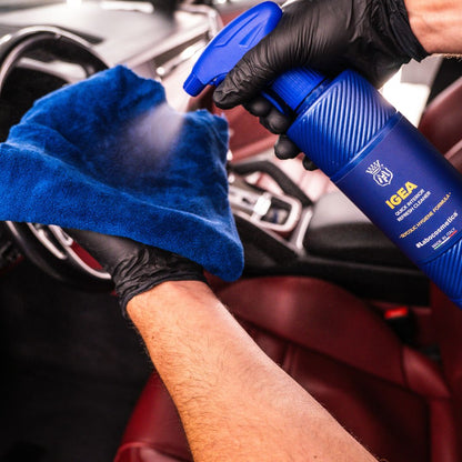 Person cleaning car interior with a Labocosmetica IGEA and blue microfibre cloth, wearing black gloves.