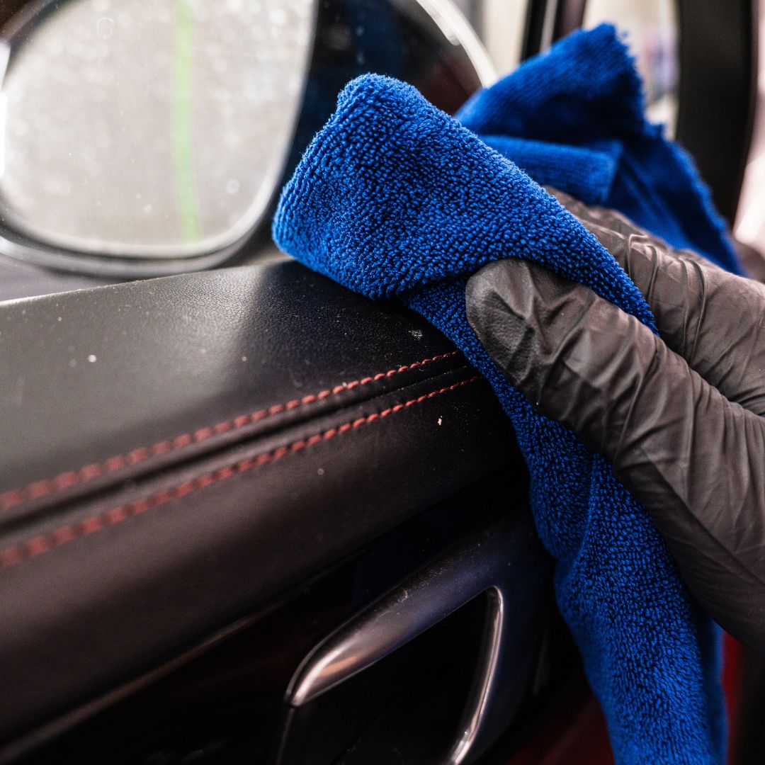 Person cleaning car interior with a blue microfiber cloth and black glove
