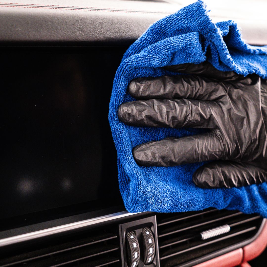 Person cleaning a car infotainments screen with a blue microfibre IDEALE and black gloves