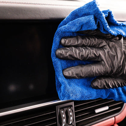 Person cleaning a car infotainments screen with a blue microfibre IDEALE and black gloves