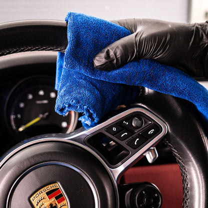 Person cleaning a car's dashboard with a blue microfibre and black gloves