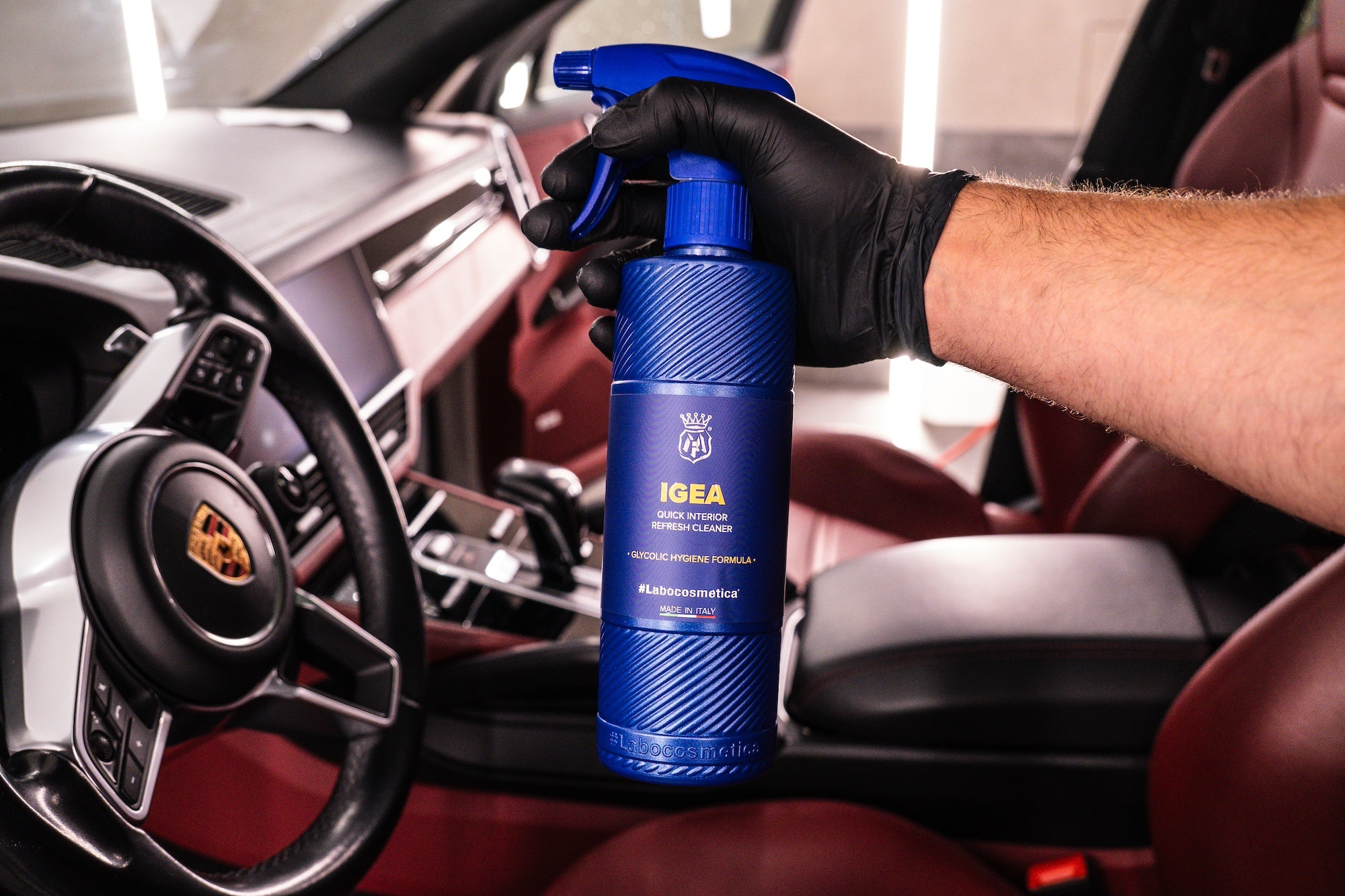 Person holding a blue Labocosmetica bottle labeled 'IGEA' inside Porsche Panamera.