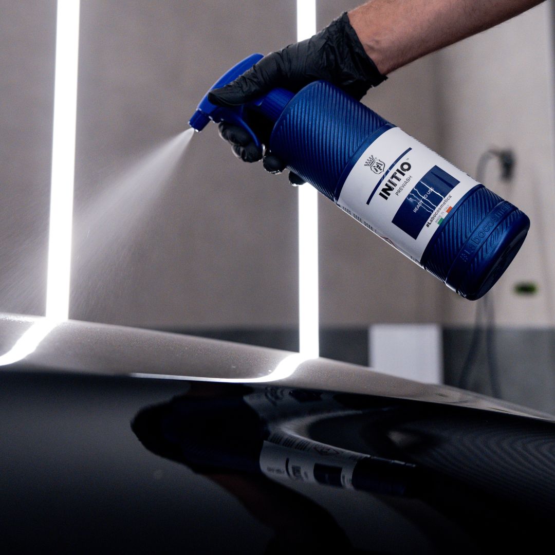 Person using a blue spray bottle labeled 'INITIO' on a reflective surface.