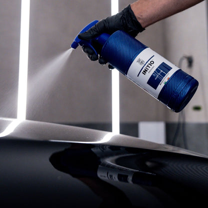 Person using a blue spray bottle labeled 'INITIO' on a reflective surface.