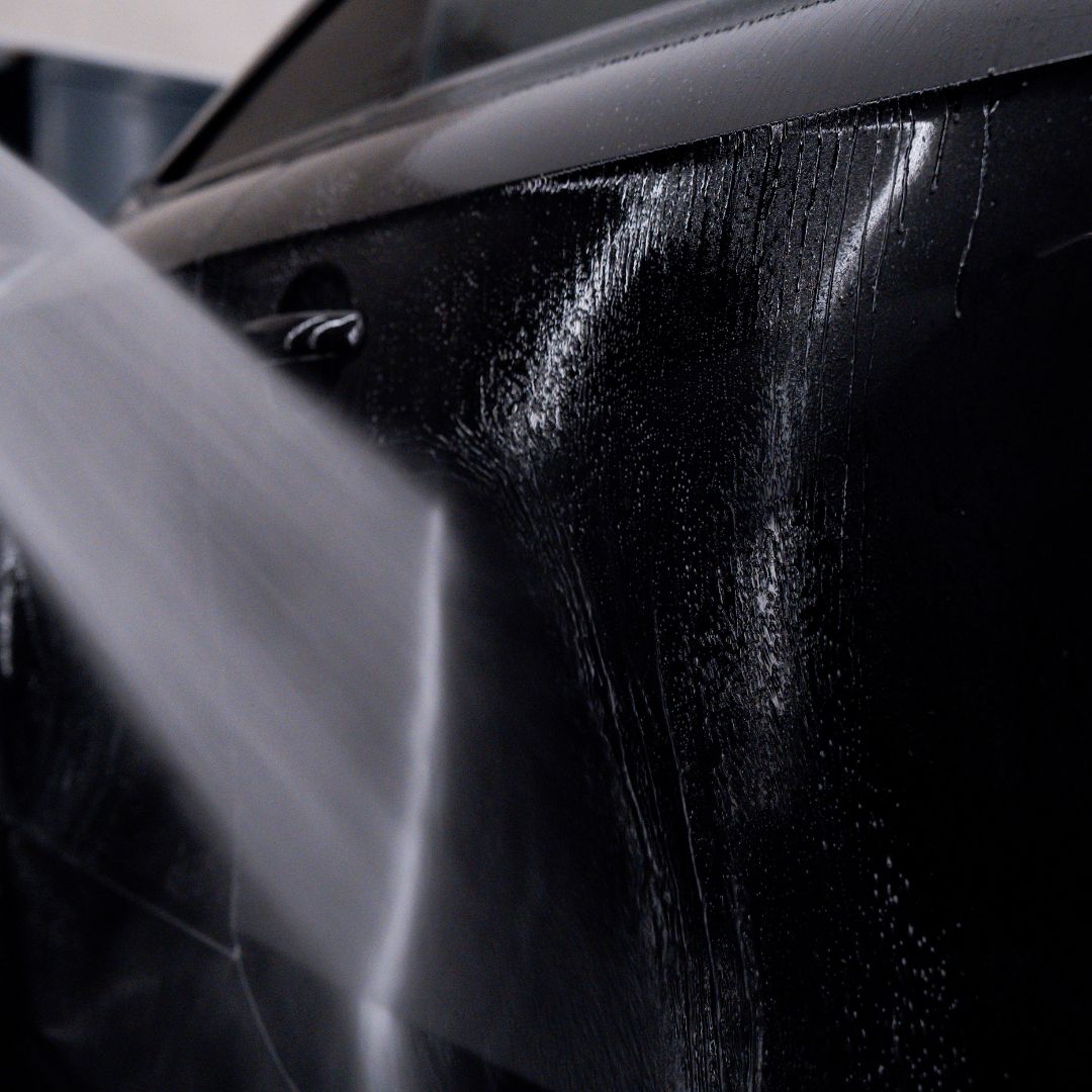 Close-up of a black car door with water droplets on a blurred background