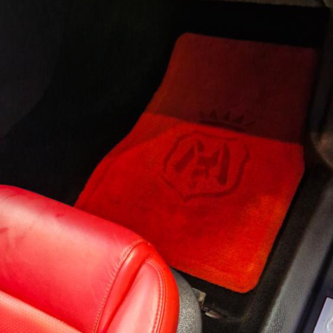 A red Porsche car floor mat with an embossed Labocosmetica shield logo, shown installed inside a vehicle next to a red leather seat.