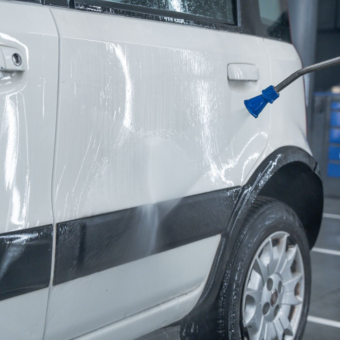 Fiat Panda being washed with a high-pressure water gun, showing water droplets on the surface.