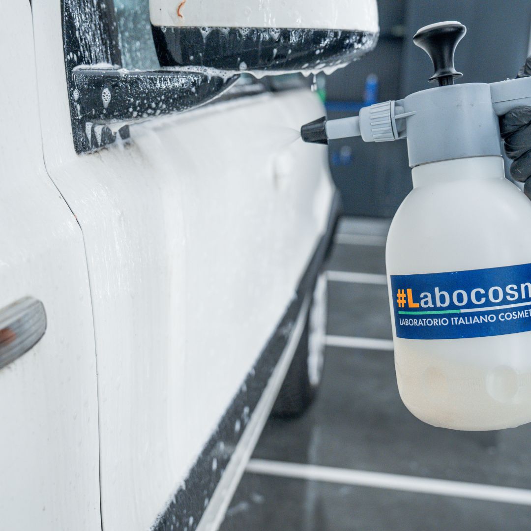 Spraying a white Fiat Panda with a bottle labeled 'Labocosmetica' in an indoor setting.