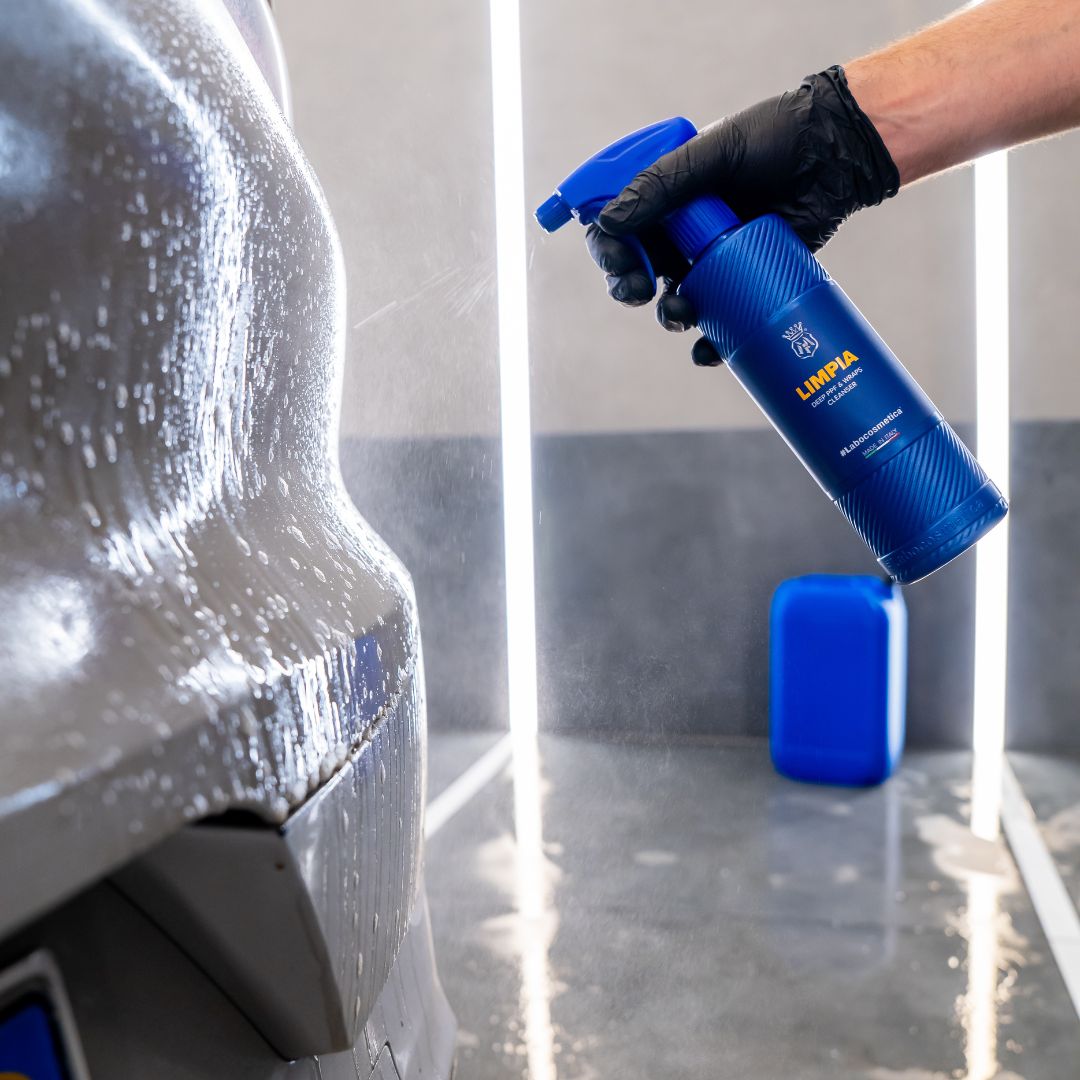 Person cleaning PPF on car with a blue spray bottle labeled 'Labocosmetica LIMPIA' in a garage setting.