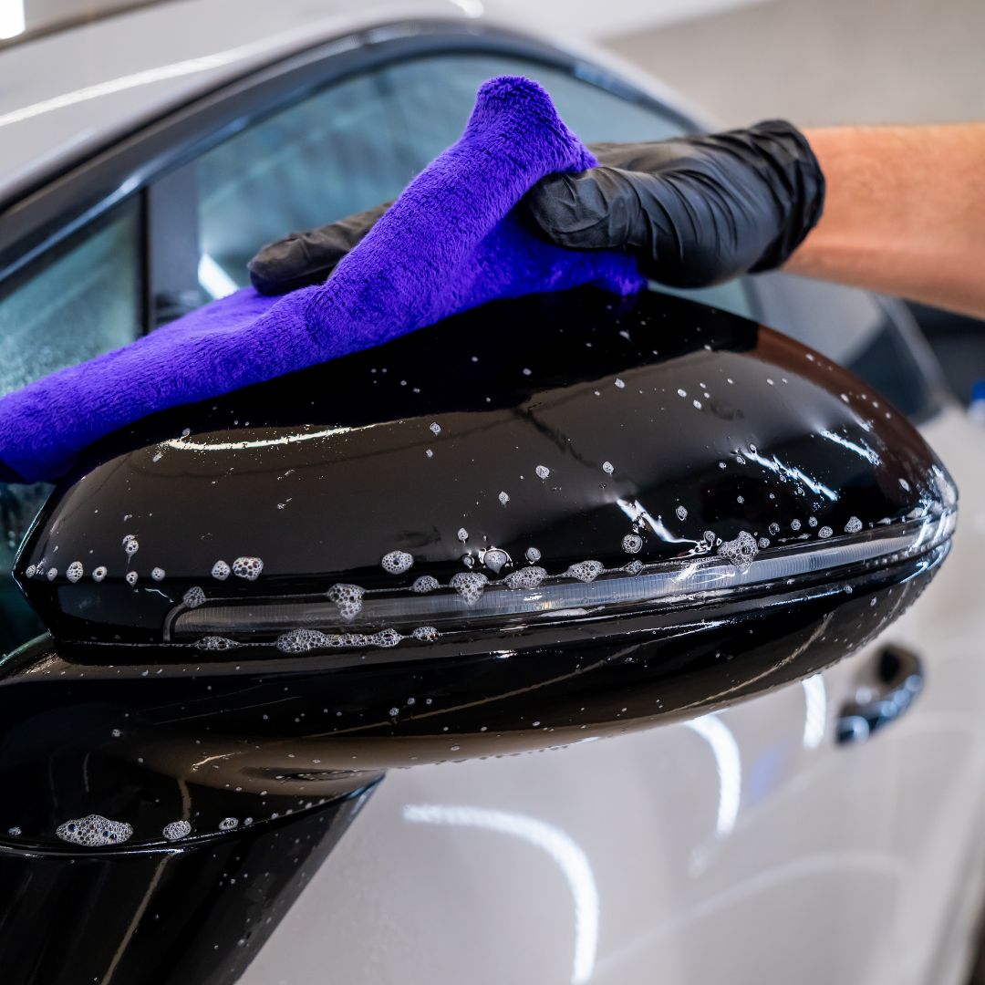 Person cleaning a PPF car mirror with a purple towel and black gloves.