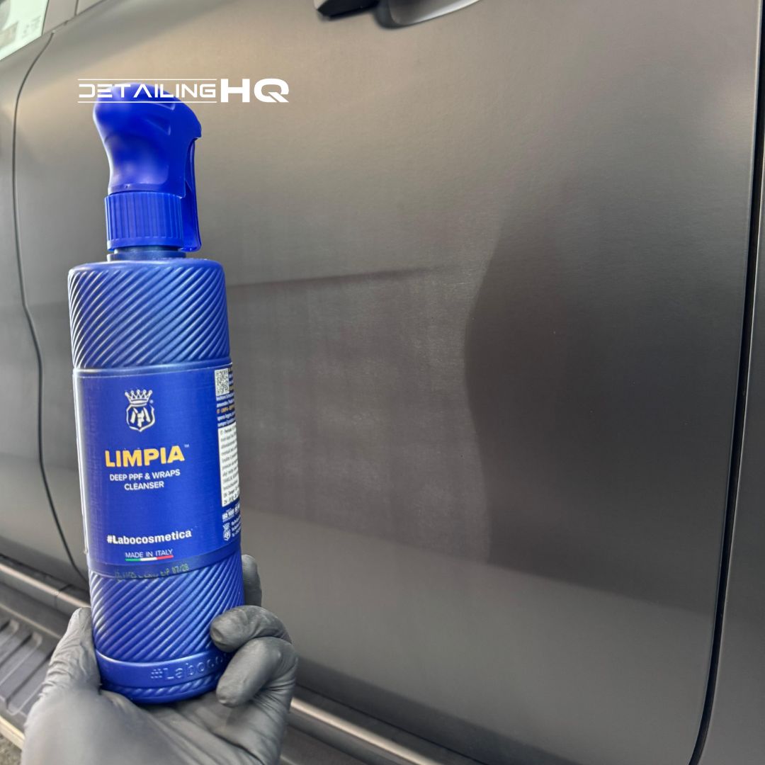 Blue bottle of LIMPIA car cleaning product held by a gloved hand against a car background.
