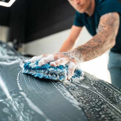 Person cleaning a car bonnet with a blue wash mitt.