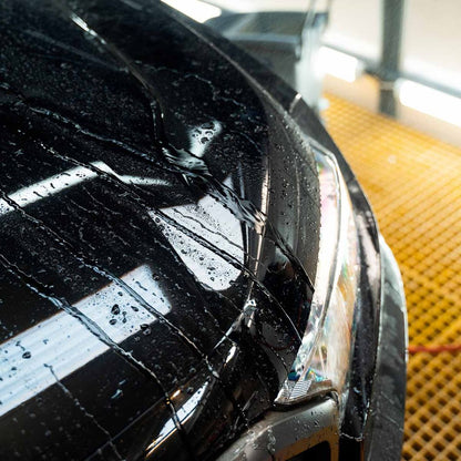 Close-up of a car's headlight and bonnet with water droplets in a car wash bay