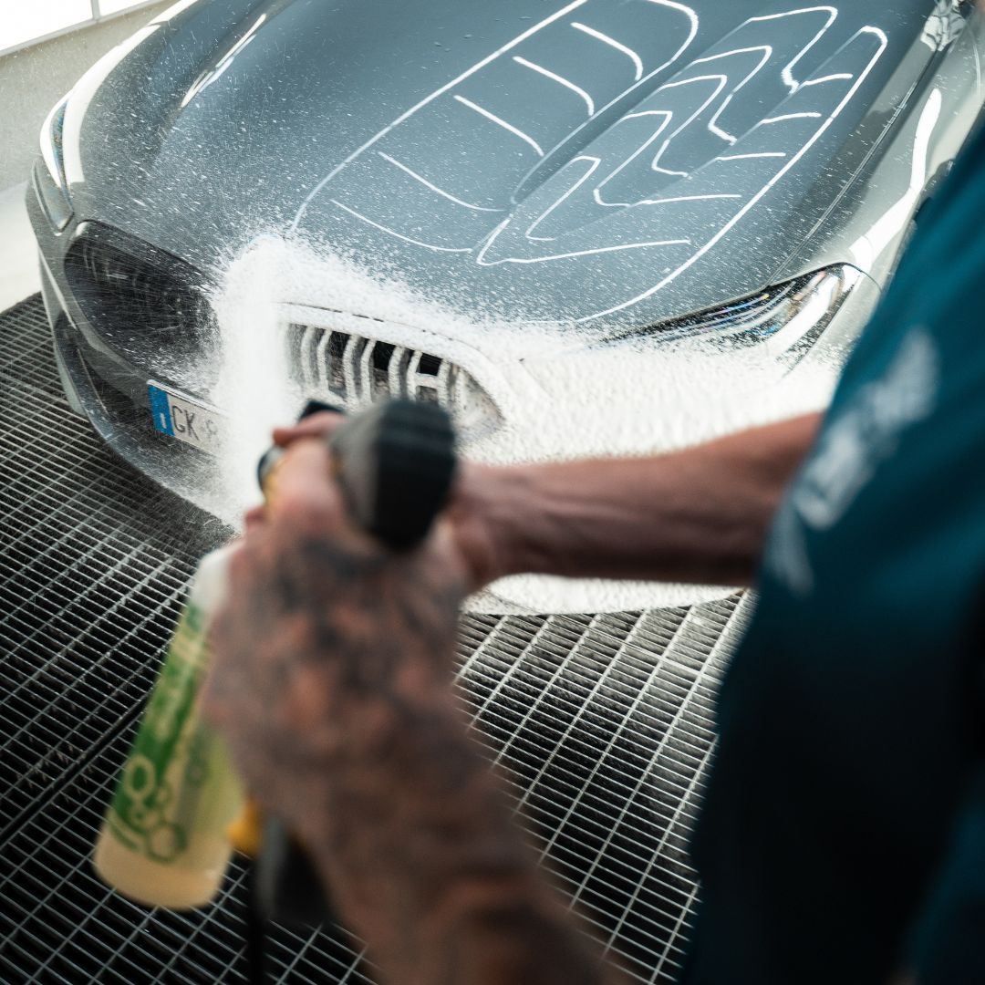 Person snow foaming a BMW with a snow foam lance using Labocosmetica Purifica Acid shampoo, focusing on the front grille.