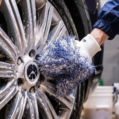 A close-up of a hand washing a silver car wheel with soapy water, wearing a blue and white microfibre cleaning glove by Labocosmetica