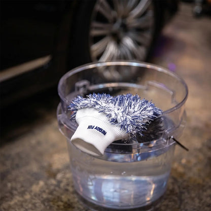 A car wash mitt glove from Labocosmetica with Reggy Fox, featuring a navy blue and white shaggy scrubber top on a white knit cuff hanging over the edge of a see through wash bucket