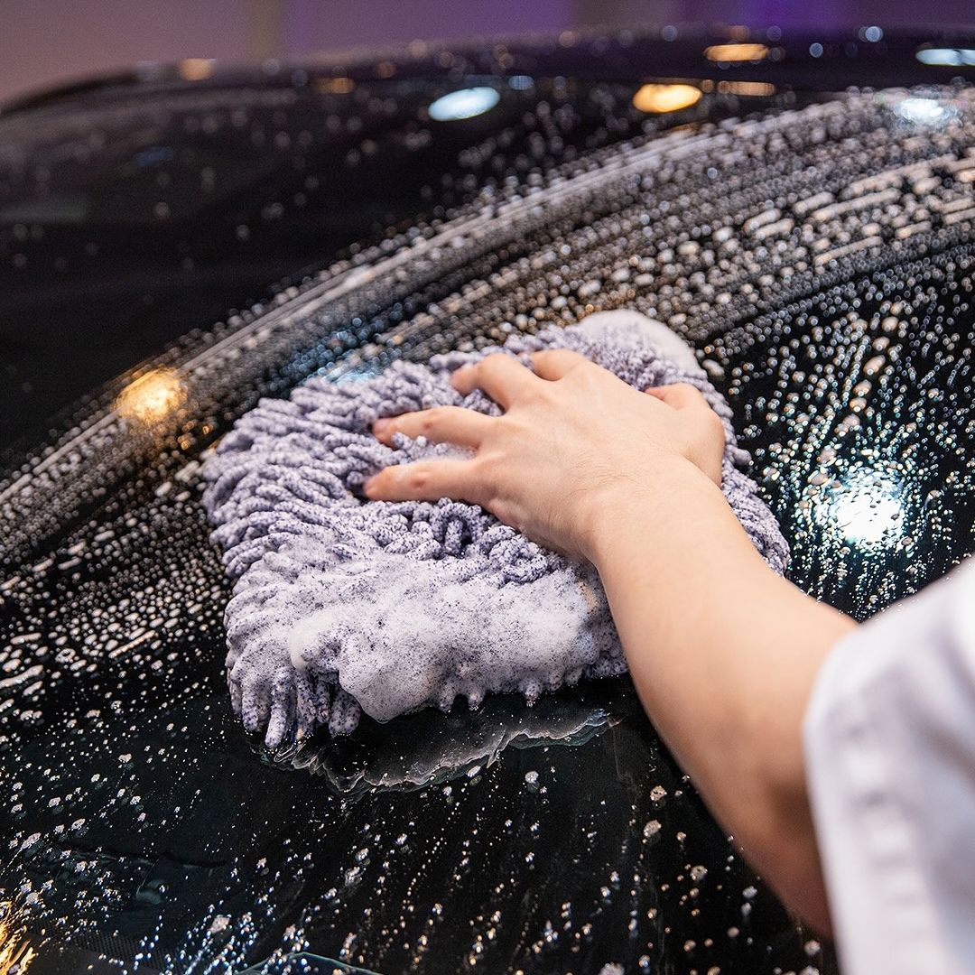 A close-up of a person's hand and arm wiping a wet, soapy black car hood with Labocosmetica Reggy Wash Pad