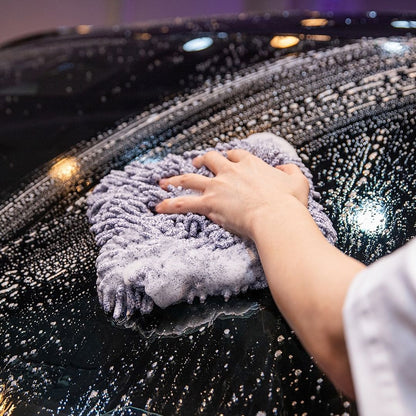 A close-up of a person's hand and arm wiping a wet, soapy black car hood with Labocosmetica Reggy Wash Pad