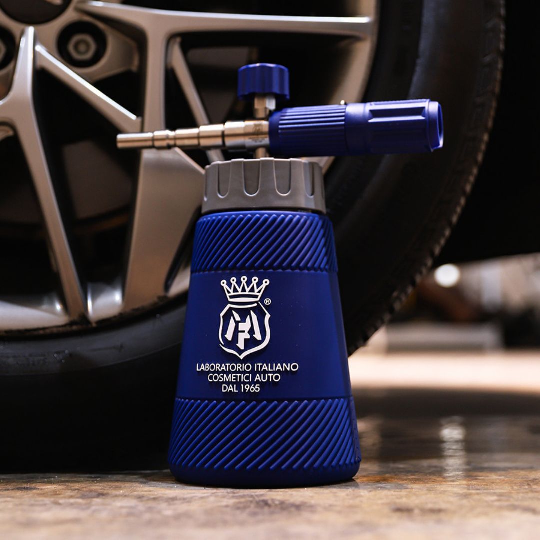 A blue and grey a Labocosmetica Snow Foam Lance with a metallic nozzle, featuring the white logo, positioned in front of a car wheel on a concrete floor.
