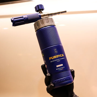 A person wearing a black glove holds a Purifica Contaminant Removal + Acids 400ml portable Labocosmetica bottle against a warm beige background.