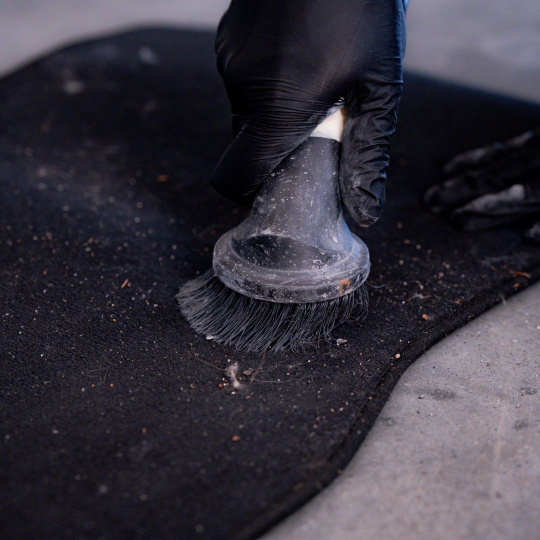 Person cleaning a black mat with a hoover vacuum wearing black gloves.