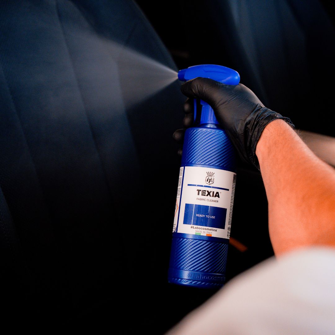 Person using a blue Labocosmetica Texia spray bottle on a fabric seat 