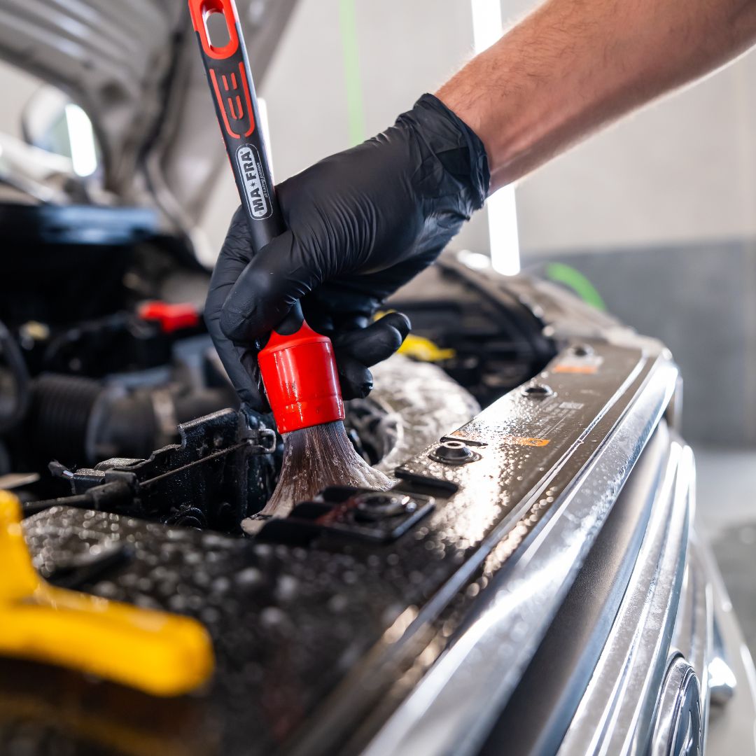 Person cleaning car engine with a brush and black gloves