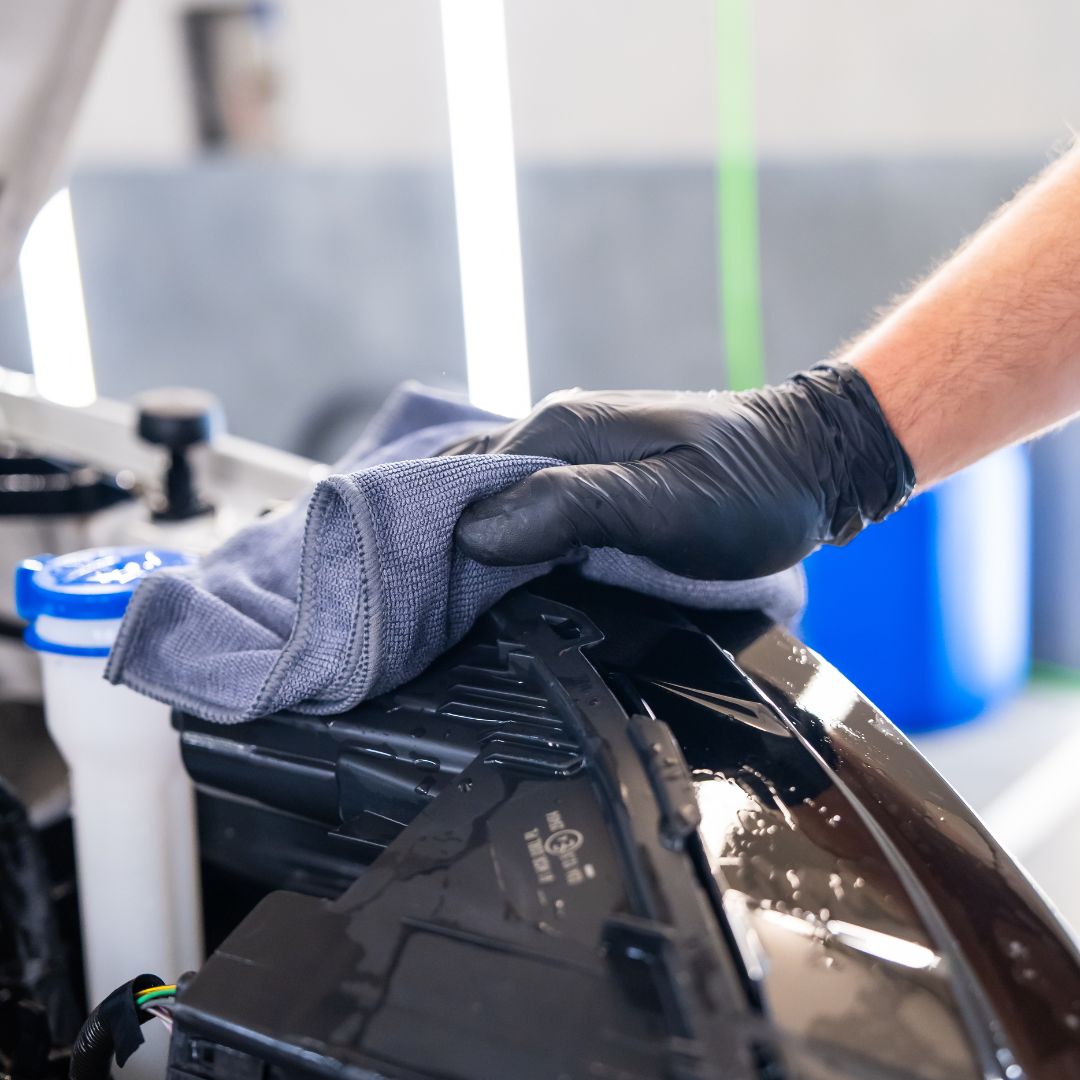 Person cleaning a car's engine bay with a cloth in a workshop setting.