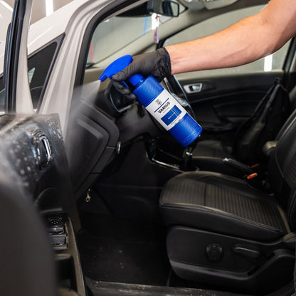 Person cleaning car interior with a blue spray bottle Labocosmetica Varius APC, wearing a black glove.