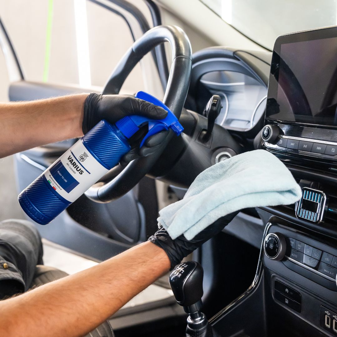 Person cleaning car interior with a spray bottle and cloth, wearing gloves.