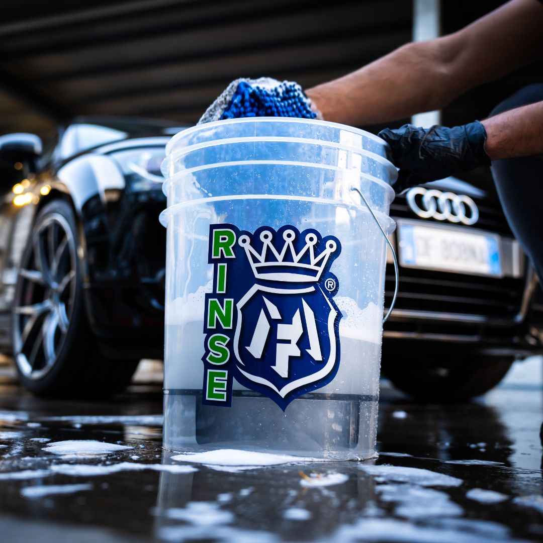 Clear Labocosmetica bucket labeled 'RINSE' with a blue sponge, car wash setting with Audi vehicle in background
