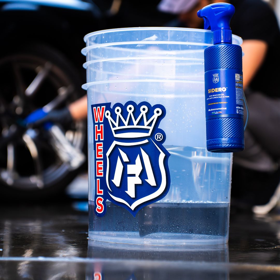 Clear Labocosmetica bucket with a blue and red Wheels sticker, a blue bottle, and a car wheel in the background.