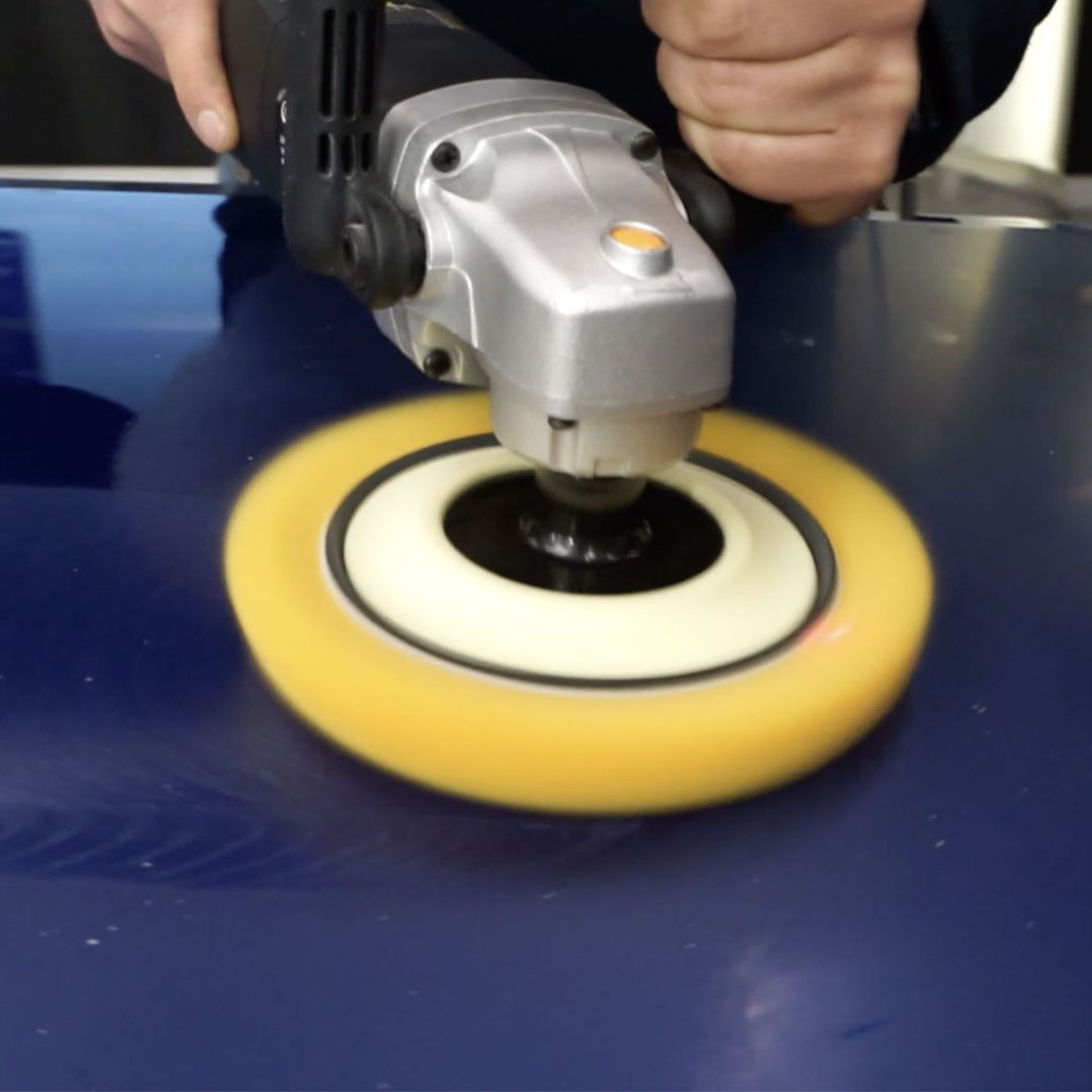 Person using a polisher on a blue car bonnet with a golden, heavy cut wool pad and ShineMate rotary polishing machine