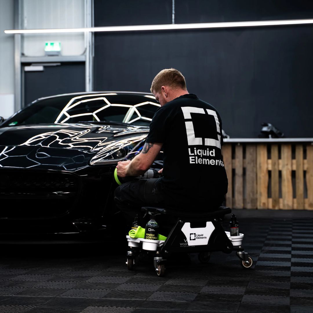 Person working on a black car with 'Liquid Elements' branding in a garage.