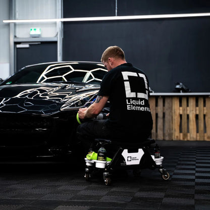 Person working on a black car with 'Liquid Elements' branding in a garage.