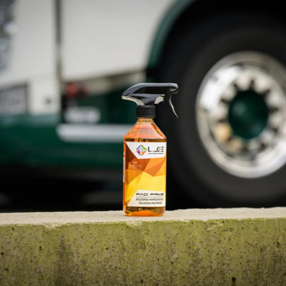 Orange spray bottle Liquid Elements Pad Prime with black nozzle on a concrete ledge with a blurred vehicle in the background