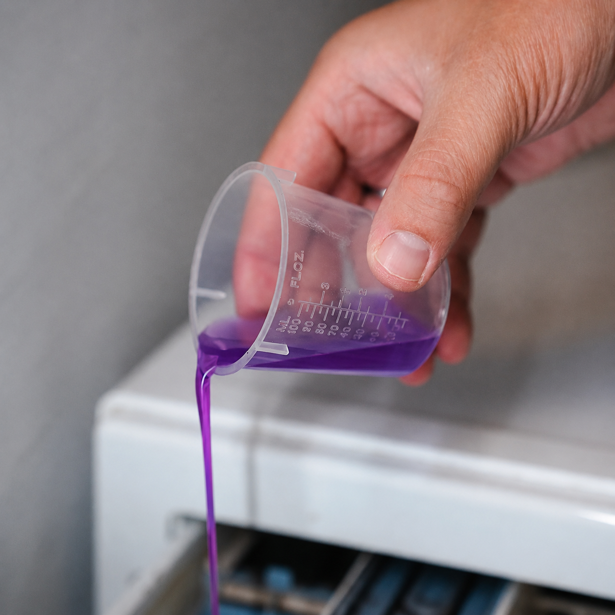 Hand pouring purple Liquid Elements towel reset liquid from a measuring cup into a machine.