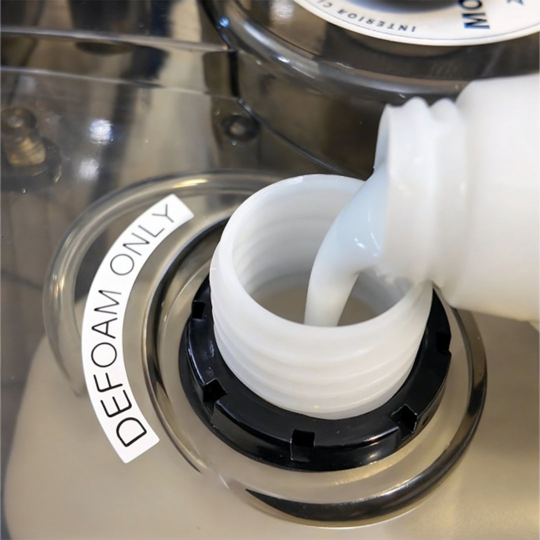 White liquid being poured into a machine with a 'DEFOAM ONLY' label.