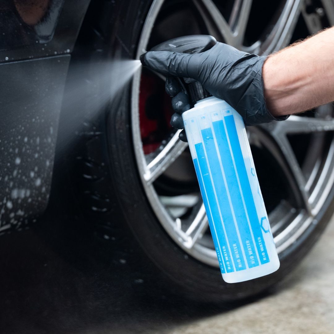Person cleaning a car wheel with a blue bottle of cleaning solution.