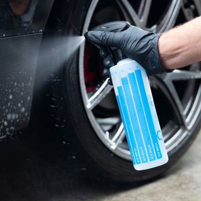 Person cleaning a car wheel with a blue bottle of cleaning solution.