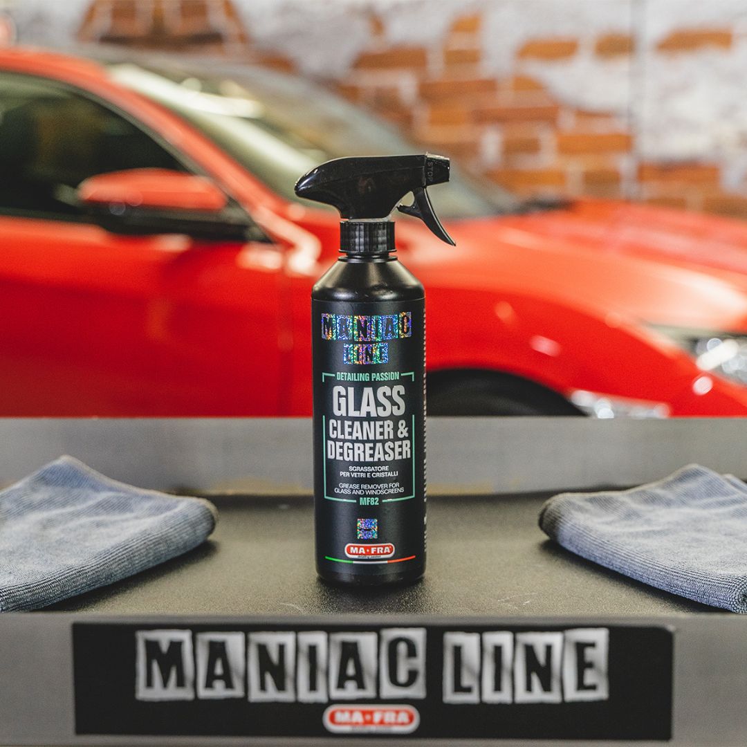 Spray bottle of Maniac Line glass cleaner and degreaser with a red car in the background.