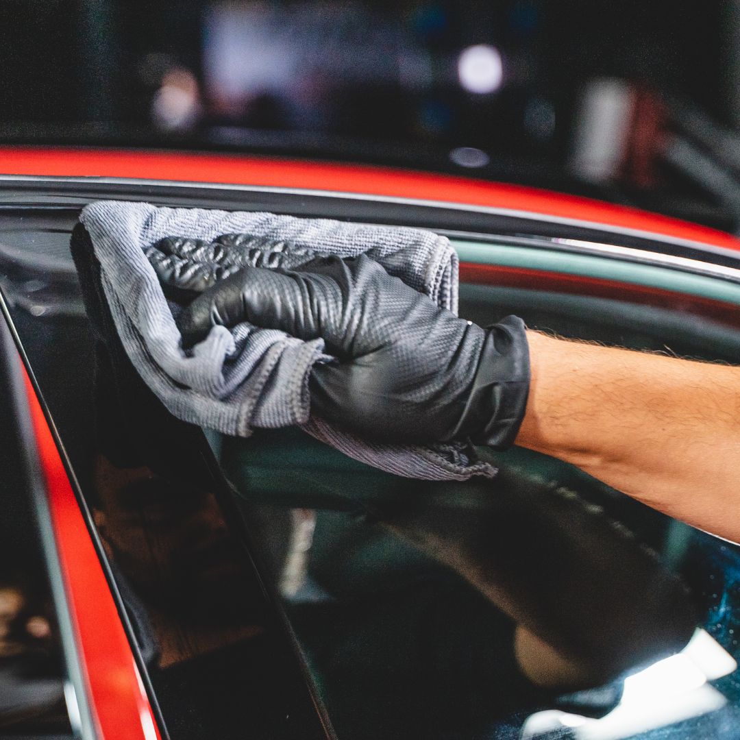 Person cleaning a car window with a cloth and black gloves.