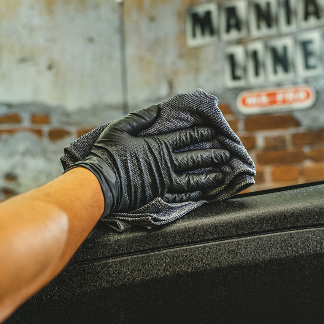 Person cleaning a car window with a black glove and gray cloth, with 'Mania Line' branding in the background.
