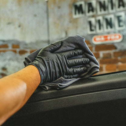 Person cleaning a car window with a black glove and gray cloth, with 'Mania Line' branding in the background.