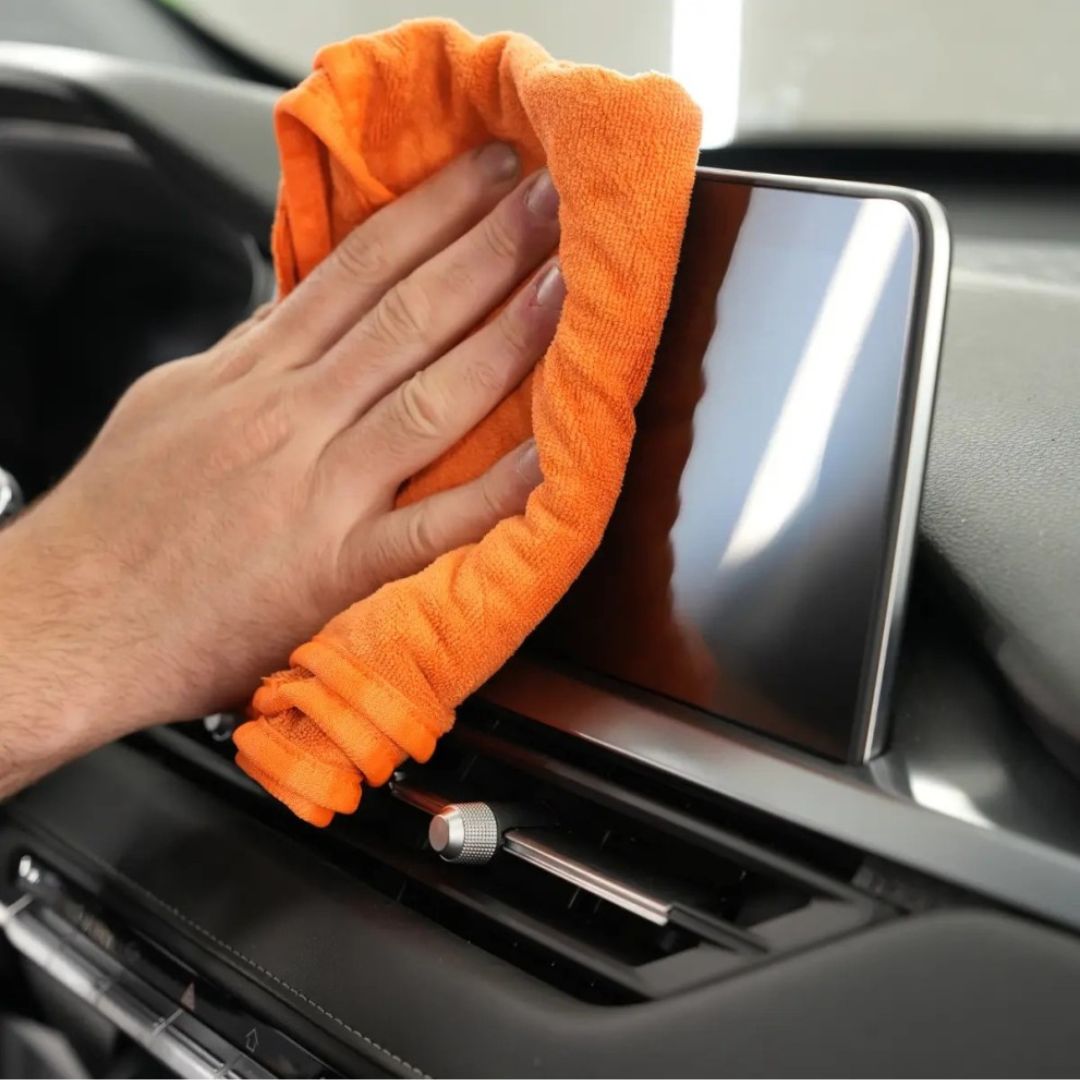 Maniac Interior Quick Detailer sprayed on an orange microfibre cloth and cleaning car infotainment screen