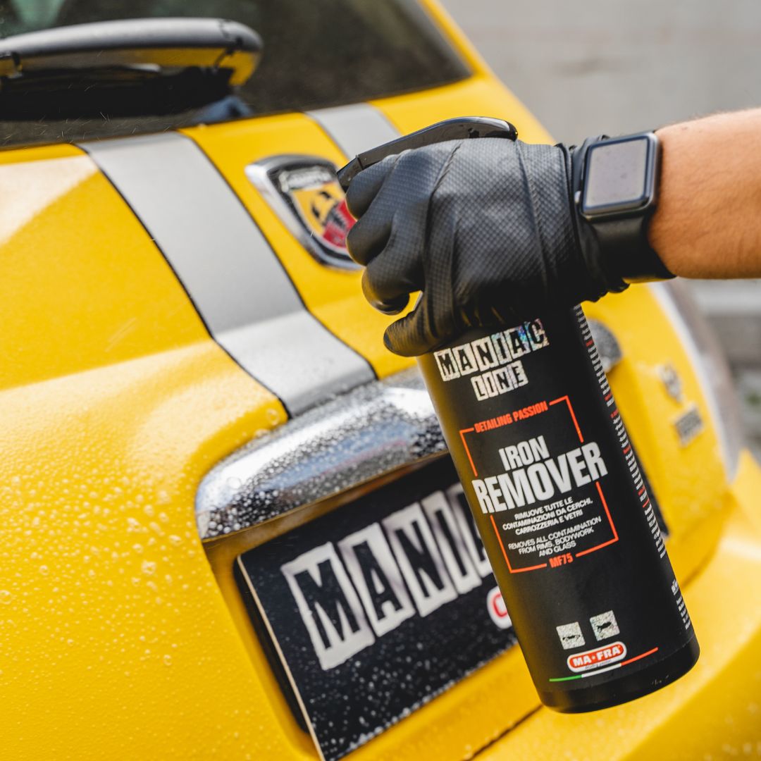 Person holding a bottle of Iron Remover spray in front of a yellow Fiat Abarth with a Maniac logo.