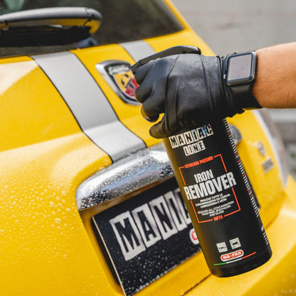 Person holding a bottle of Iron Remover spray in front of a yellow Fiat Abarth with a Maniac logo.