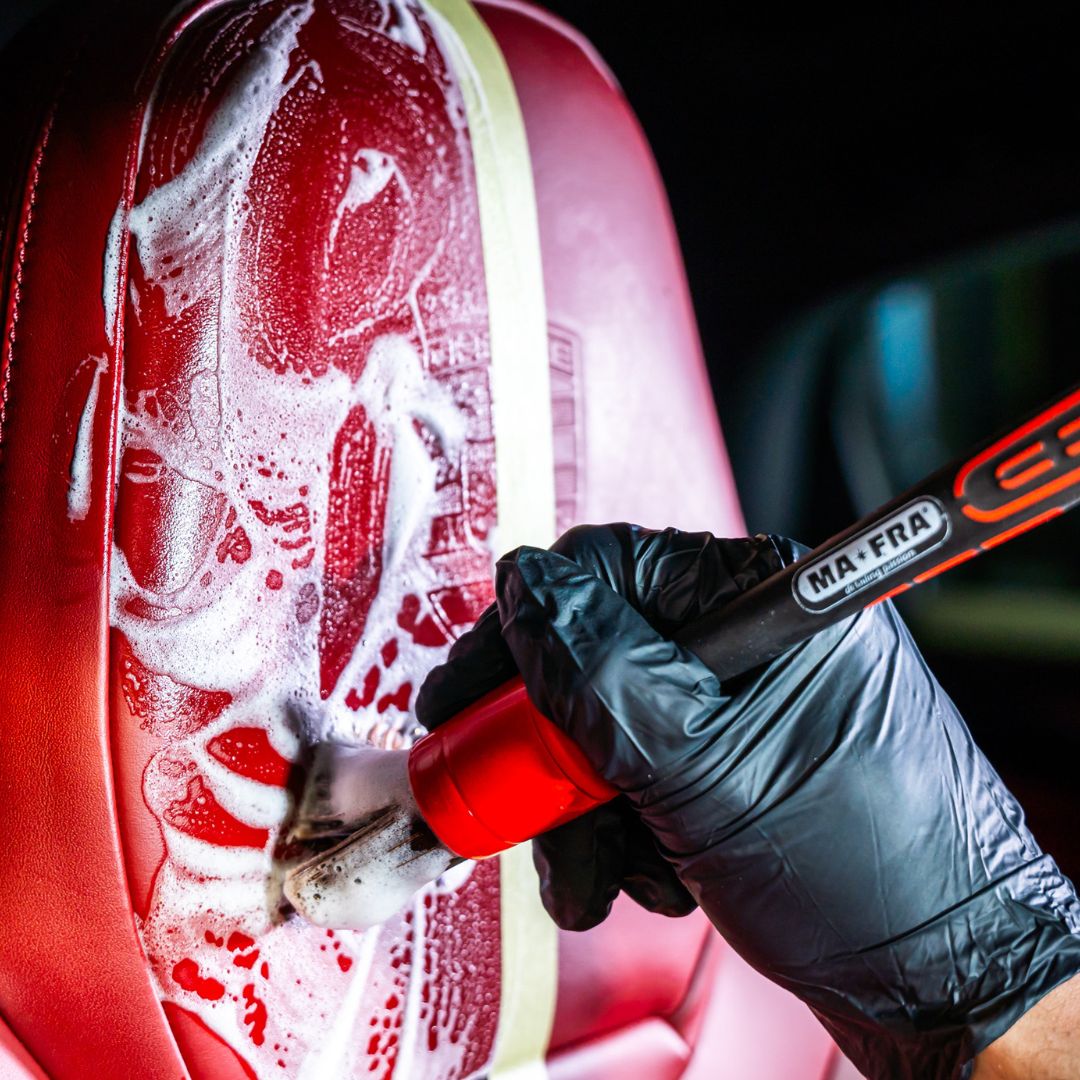 Person cleaning a red porsche car seat with a MA-FRA brush.