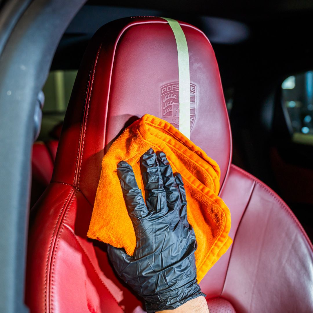 Person cleaning a red porsche leather seat with an orange cloth and black glove