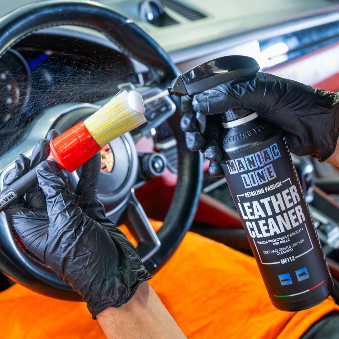 Person cleaning a car interior with Maniac leather cleaner and brush, wearing black gloves.